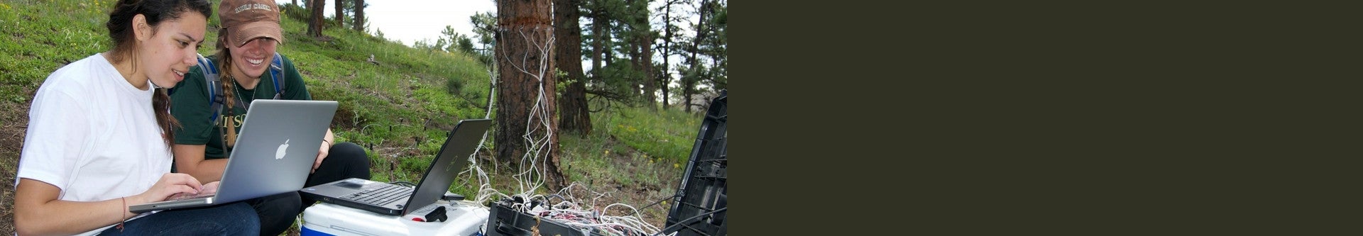 Two students working on laptops while doing fieldwork
