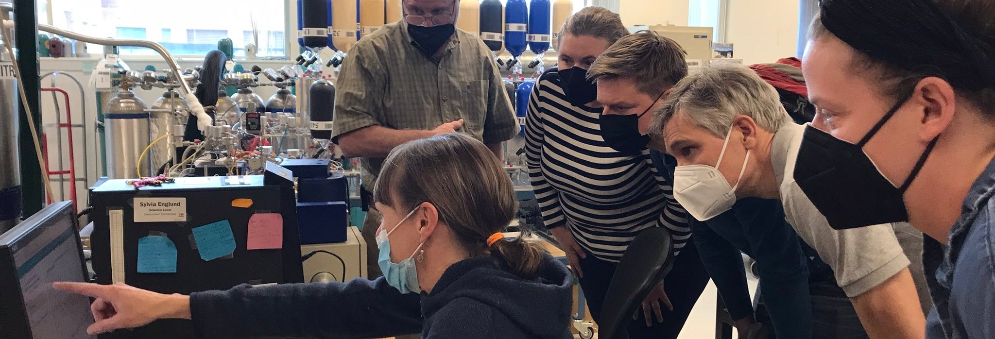  A half dozen researchers, including visitors from Finland, gather around a desktop computer to view and discuss lab measurements and data