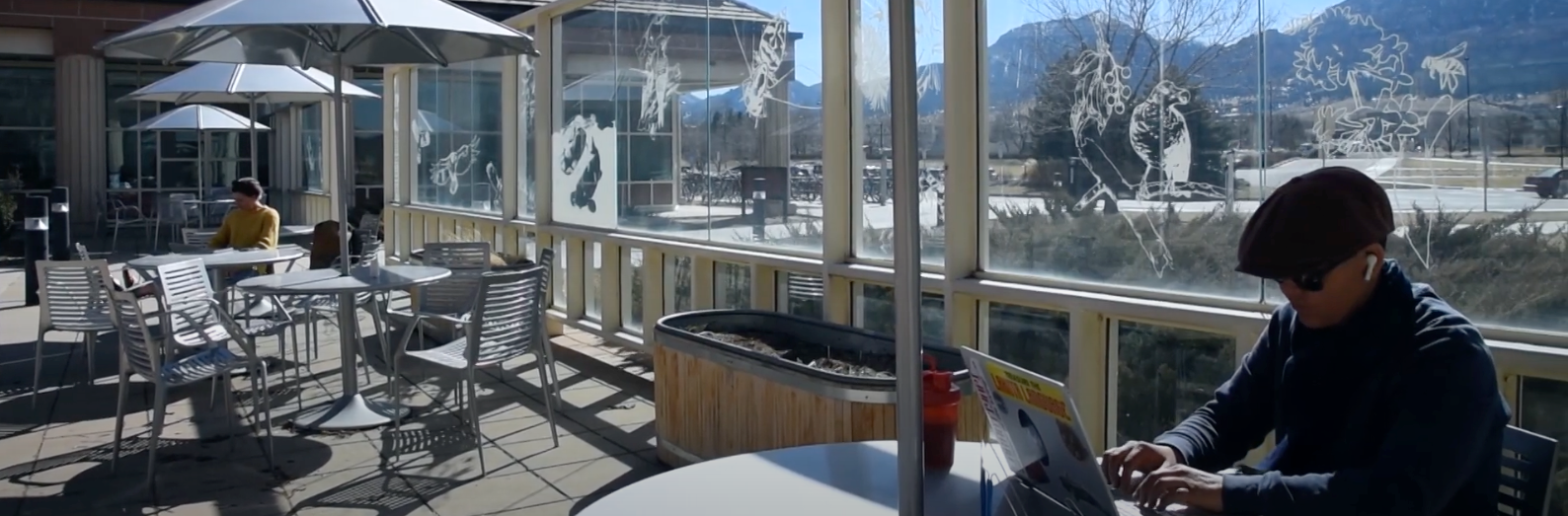 Person works at a laptop outside on the front deck of SEEC, with the flatiron mountains visible behind