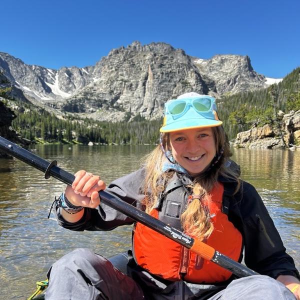 Katie Gannon paddles a small inflatable boat on a high altitude lake in the Rocky Mountains, with dramatic cliffs behind