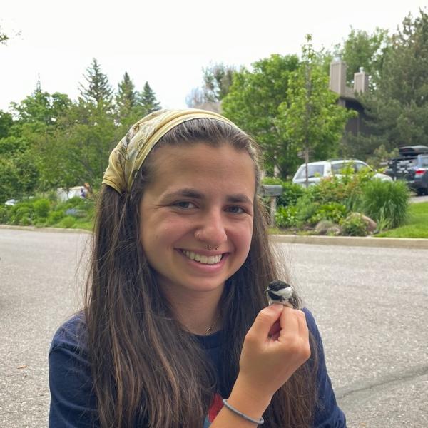 A smiling Sara Padula holds a Chickadee in her hand
