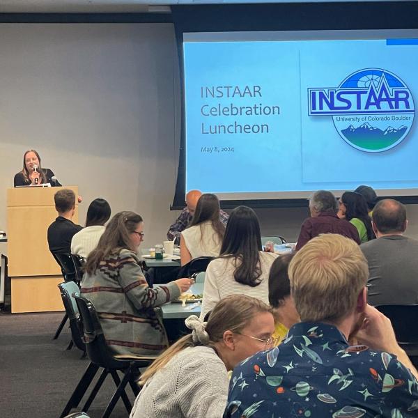 INSTAAR celebration luncheon May 8th 2024: A room full of people at tables watch Interim Director Nikki Lovenduski kick off the event.