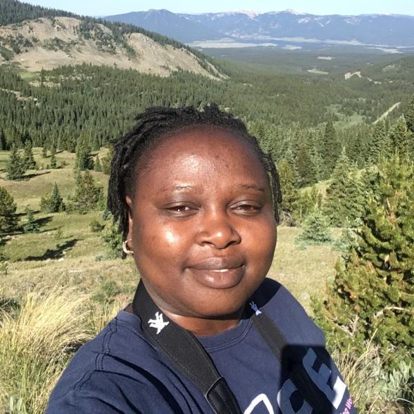 With clear blue skies, Rahila Yilangai takes a summer selfie while doing fieldwork on a forested ridge, with a broad valley below and mountain skyline of Crested Butte Colorado