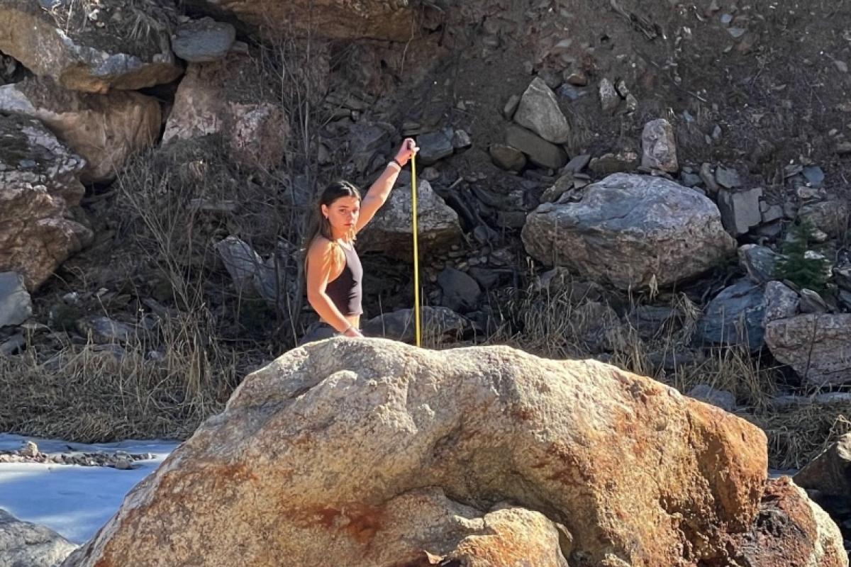 A student measures a large boulder for a Field Methods in Geomorphology course, 2025
