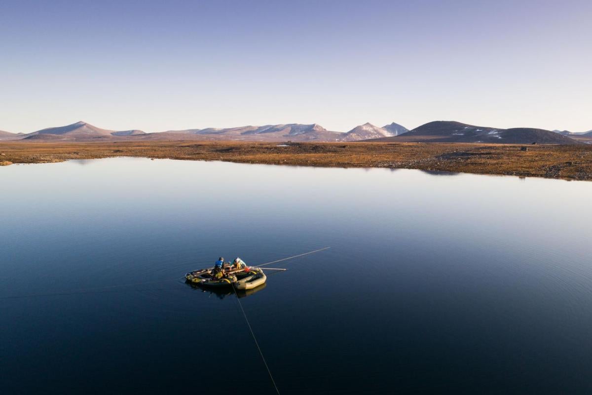 Sarah Crump and Greg de Wet maneuver their makeshift raft across a mirror-like lake on Baffin Island. Photo by Zach Montes, Orijin Media