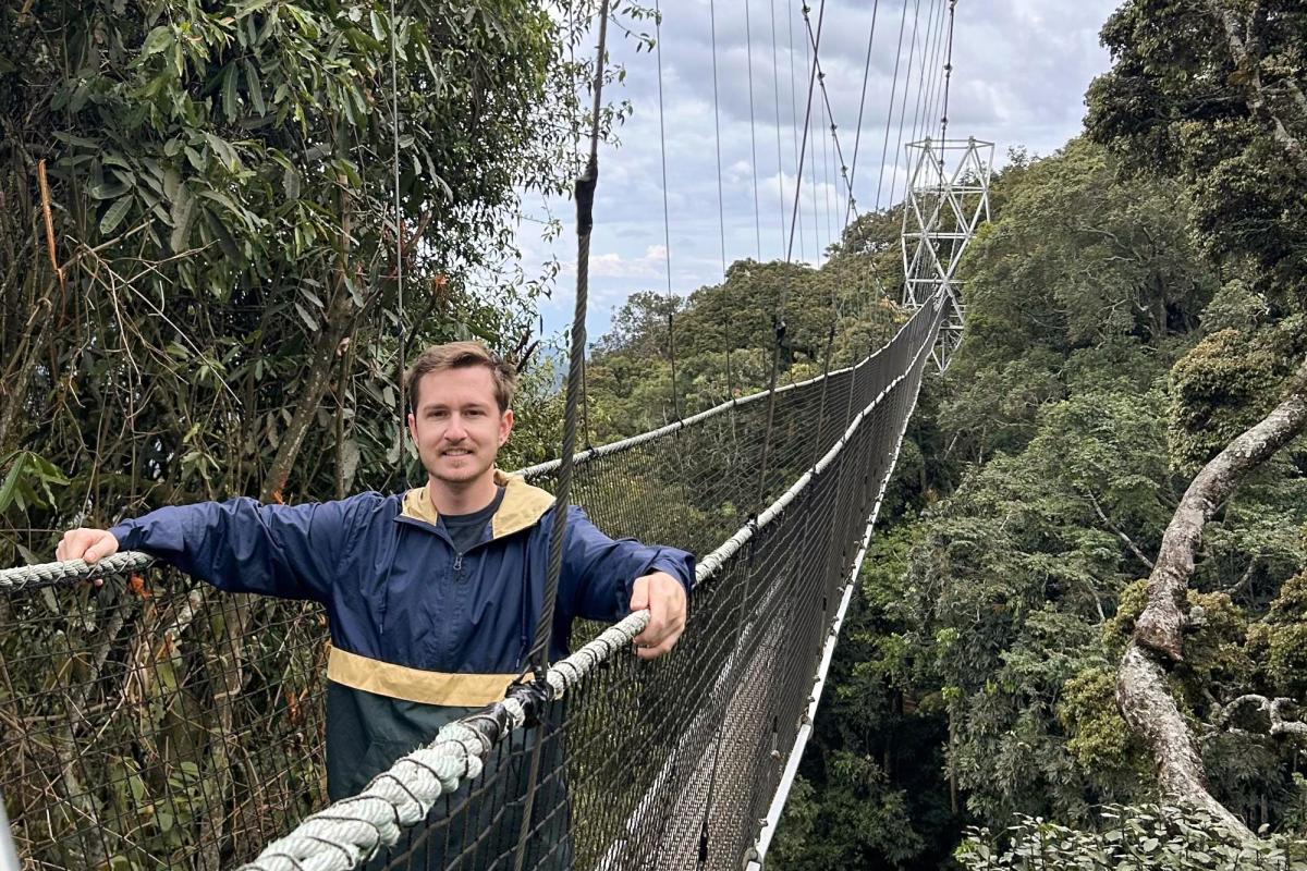 Tim Higgins hikes across a very long rope bridge at tree top level in the rainforest in Nyungwe National Park, Rwanda