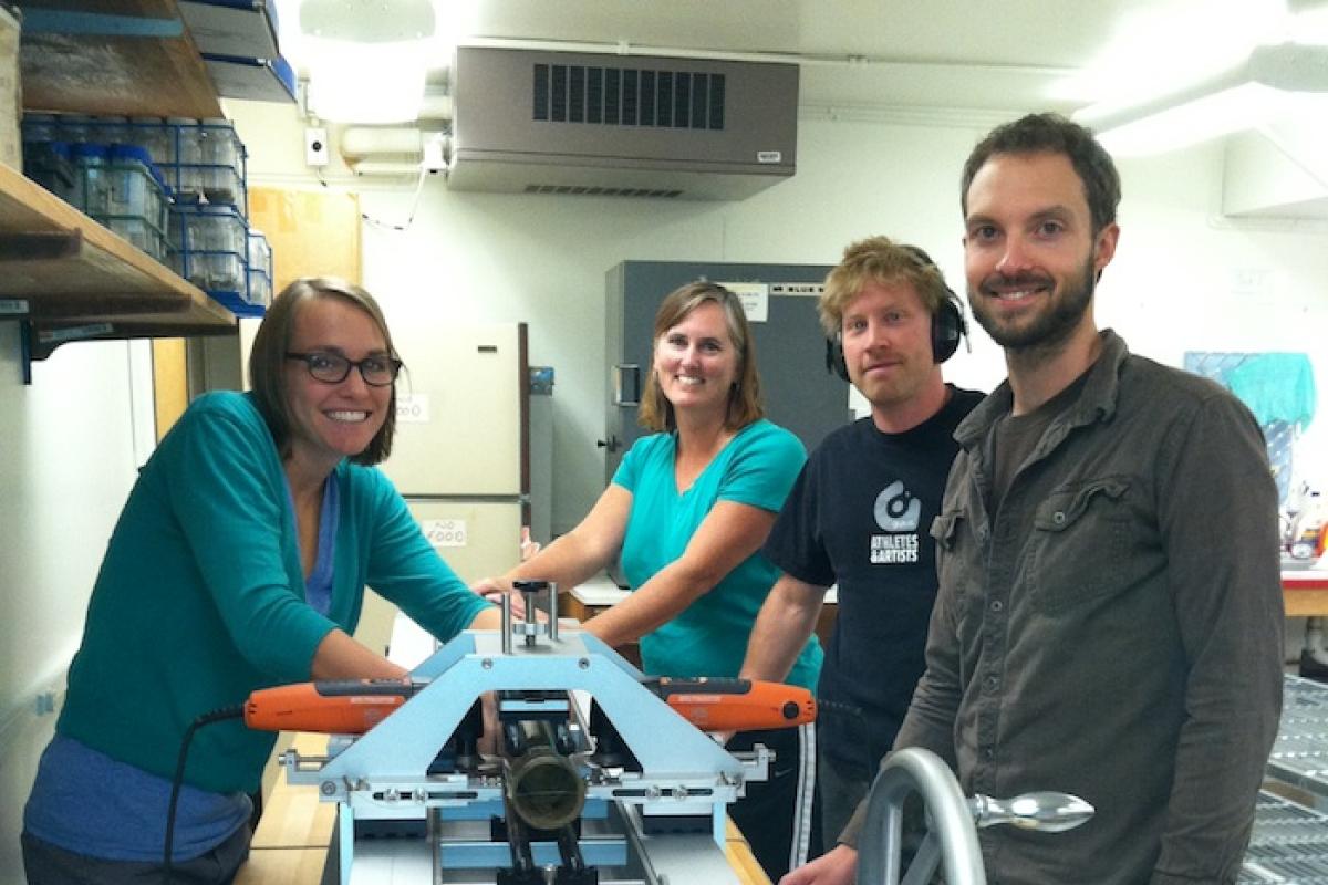 Four scientists at a lab bench split a sediment core for examination and sampling