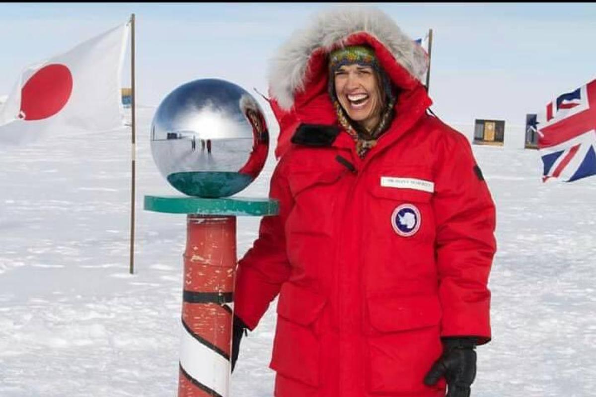 Diana Nemergut, in big red parka and furry hood, stands at the marker for Amundsen-Scott South Pole station in Antarctica
