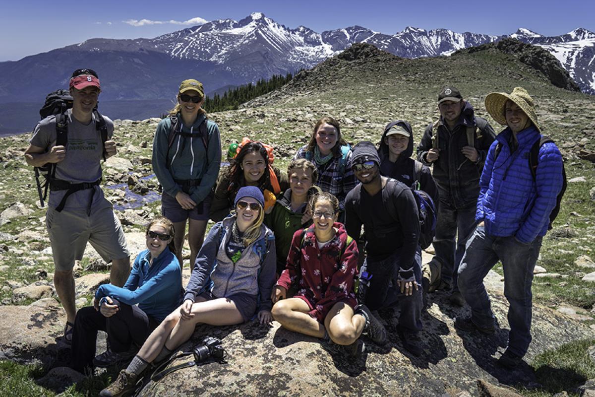 A group of undergraduate researchers pose for a big group photo with the jagged skyline of Rocky Mountain National Park in the background