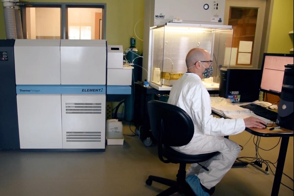 Tom Marchitto wears a tyvex suit and booties at a computer workstation adjacent to the inductively-coupled plasma mass spectrometer, a big white and gray instrument about the size of several refrigerators
