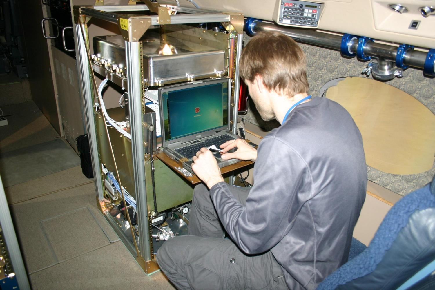 Petter Weibring sits on an airplane seat while working on a spectrometer 