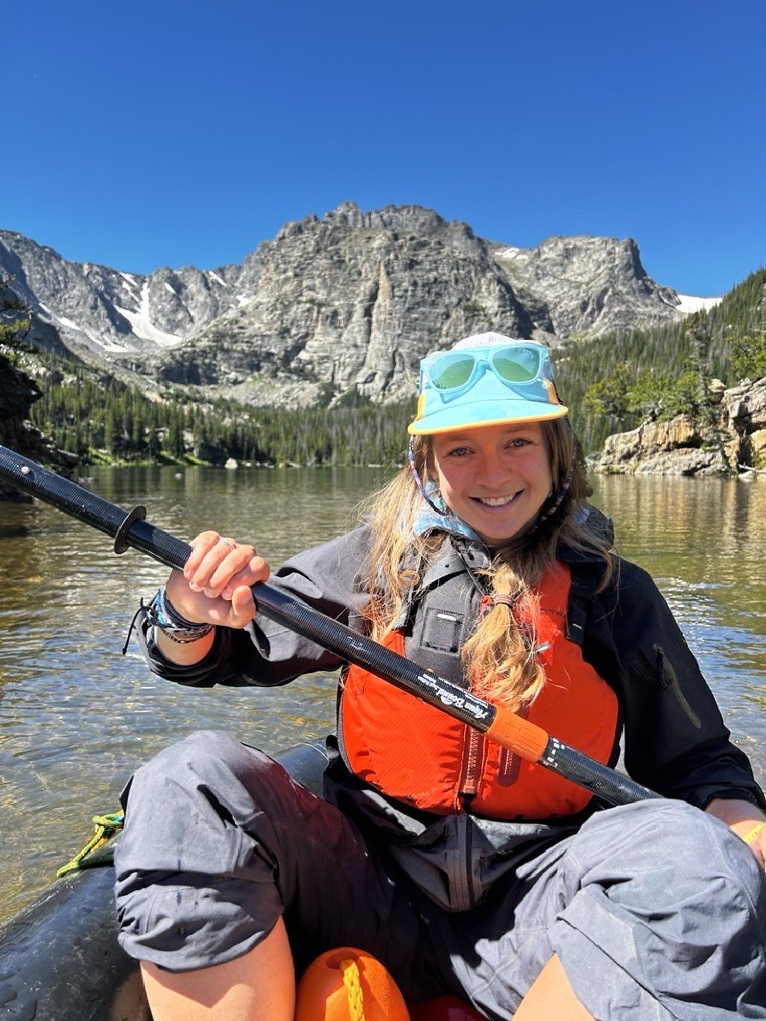 Katie Gannon paddles a small inflatable boat on a high altitude lake in the Rocky Mountains, with dramatic cliffs behind