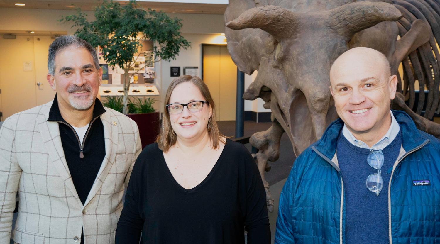 Portrait of Nicole Lovenduski, Justin Schwartz, and Massimo Ruzzene. Behind them is a Triceratops skeleton.