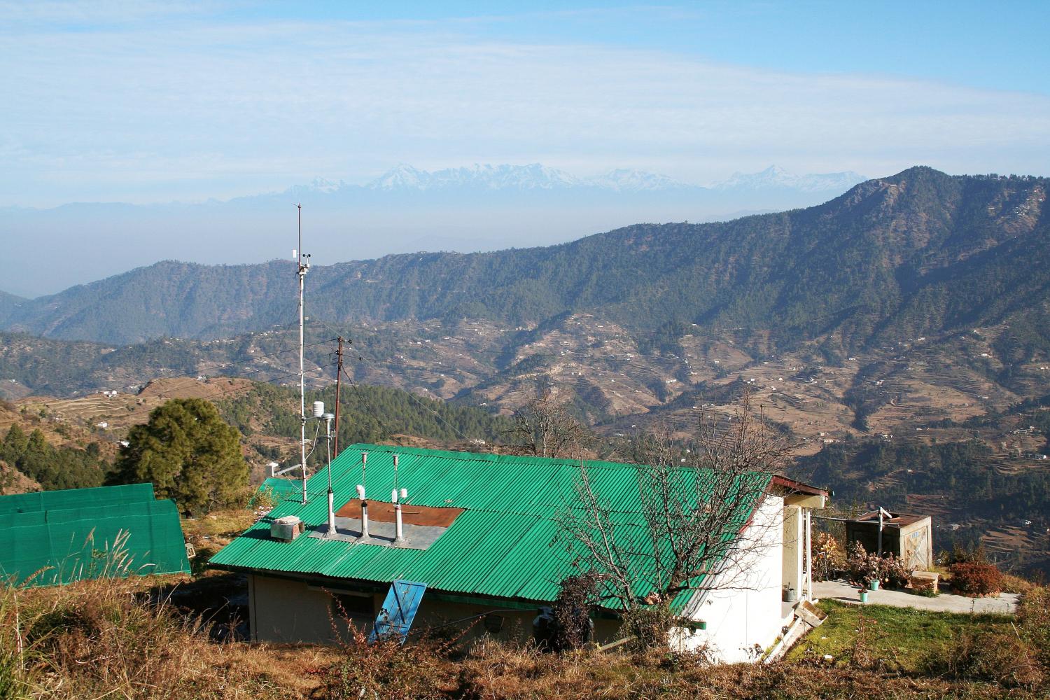 A green roofed building with attached climate and aerosol sensors sits in the Himalayan foothills, with high peaks on the skyline