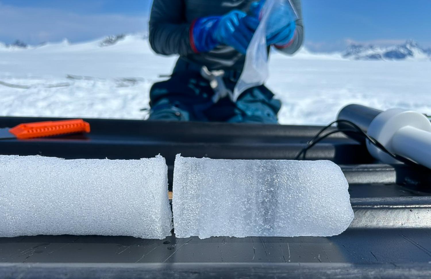 cylinders of ice rest atop a black sled while a figure in blue gloves bags up a sample in the background