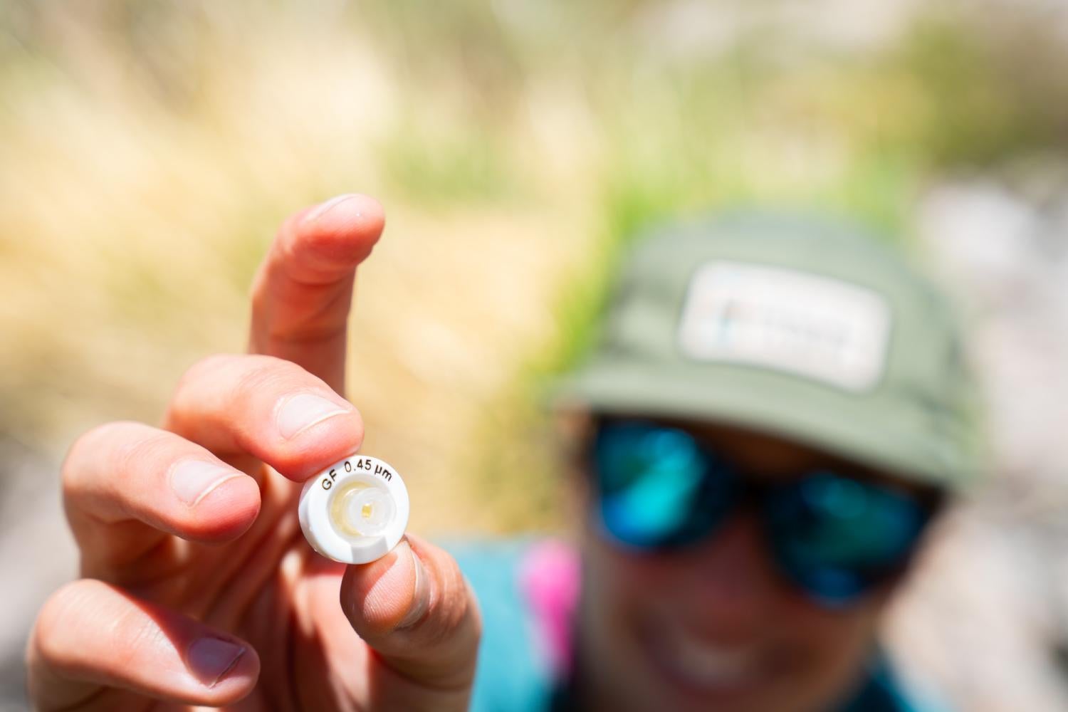 A woman holds a tiny, white circular cap with letters reading "GF 0.45 micrometers" around the outside
