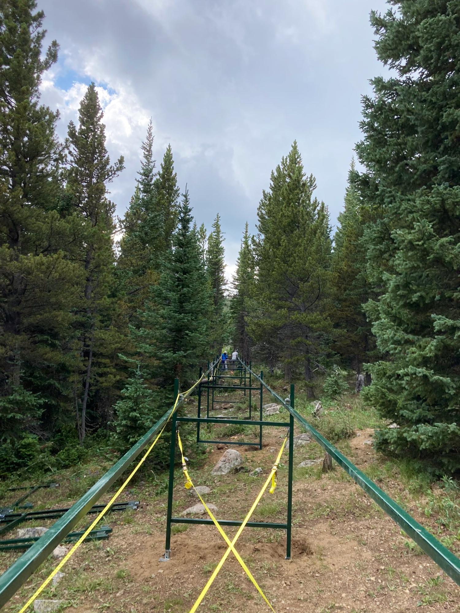 Very long green metal structure under construction in an evergreen forest will later hold an EcoTram, a moving monitoring platform focused on water, energy, & vegetation