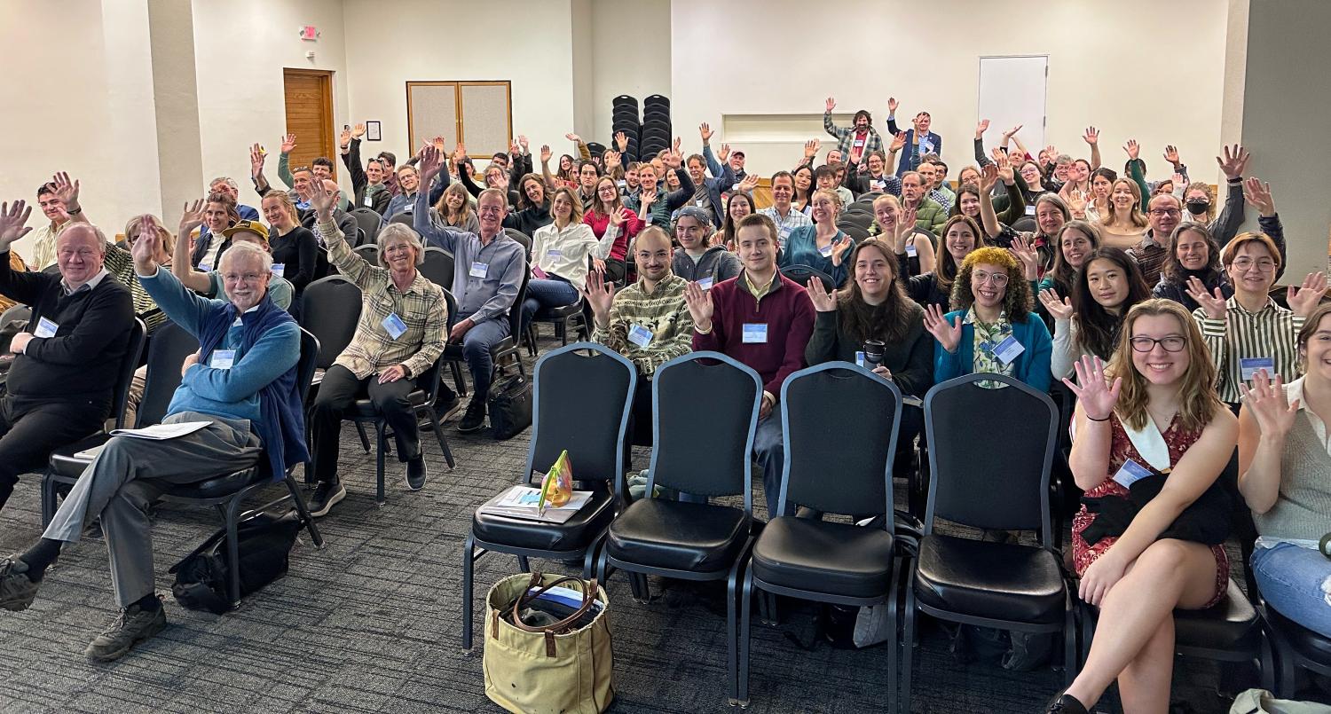 A large group of about 80 scientists wave while sitting in closely spaced chairs for the 52nd Arctic Workshop.