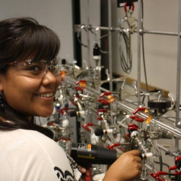 B. Skeets stands at a lab bench with lots of tubes, clamps, and equipment. She is extracting water from soil and xylem samples using a cryogenic vacuum distillation line.