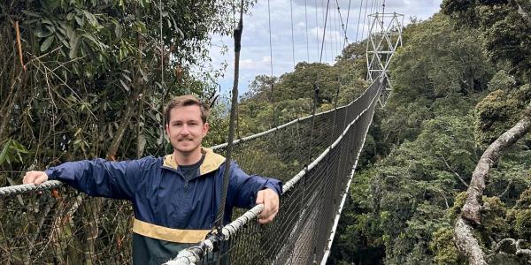Tim Higgins hikes across a very long rope bridge at tree top level in the rainforest in Nyungwe National Park, Rwanda