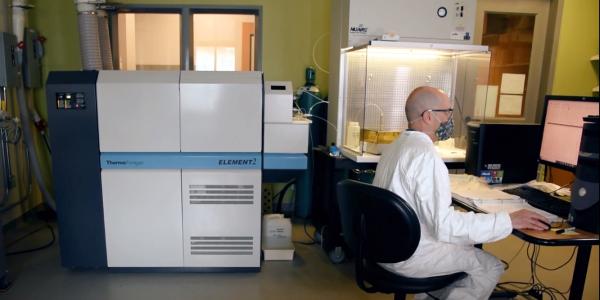 Tom Marchitto wears a tyvex suit and booties at a computer workstation adjacent to the inductively-coupled plasma mass spectrometer, a big white and gray instrument about the size of several refrigerators  