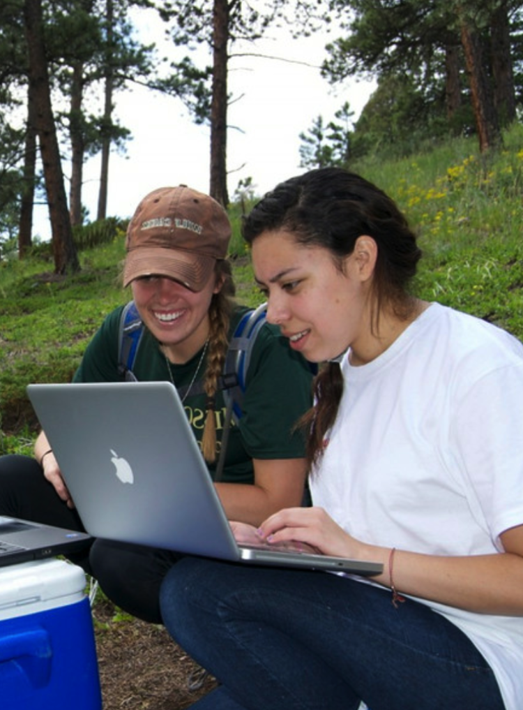 Two students use a laptop in the field to look at sensor data