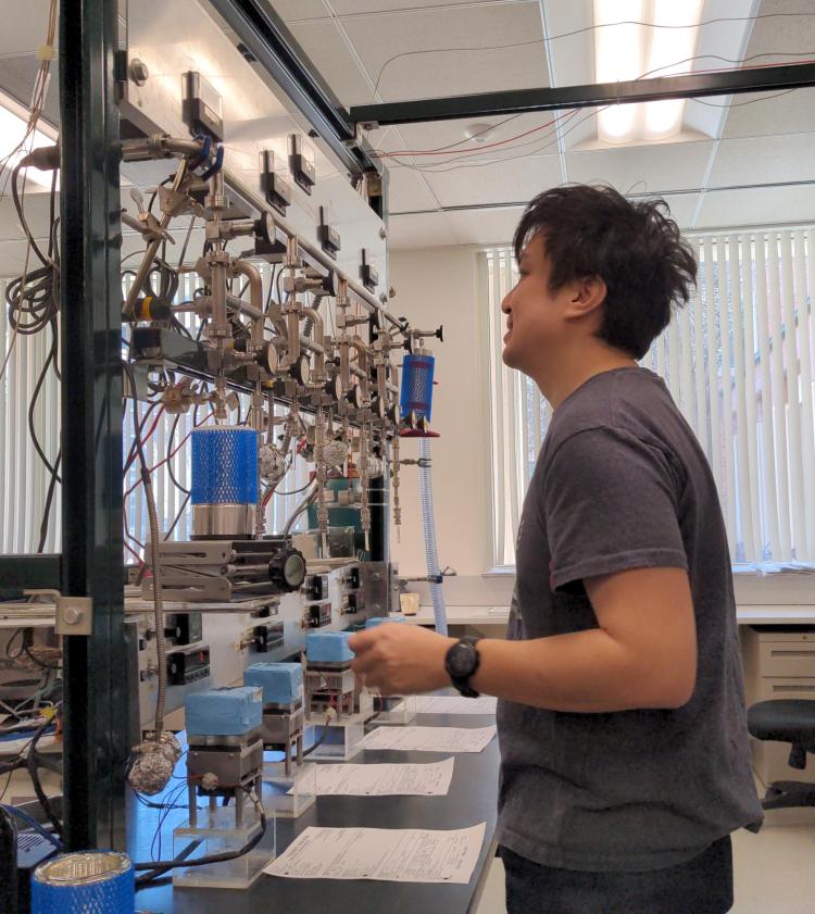 Profile view of Michael Dyonisius facing a tall rack of equipment for preparing radiocarbon samples  