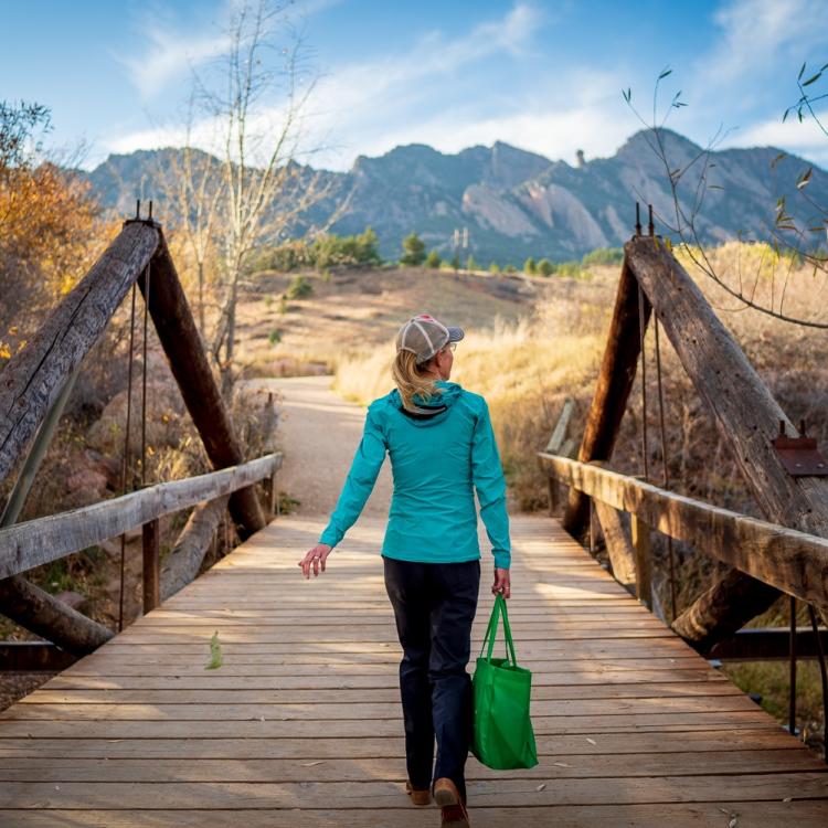 Katie Suding walks over a short wooden bridge and onto a trail heading into the dramatic cliffs of Boulder's flatirons