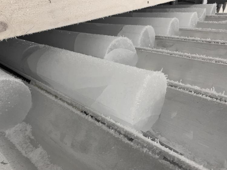 Long, arm-thick, frosty cylinders of ice lie in a grooved metal tray