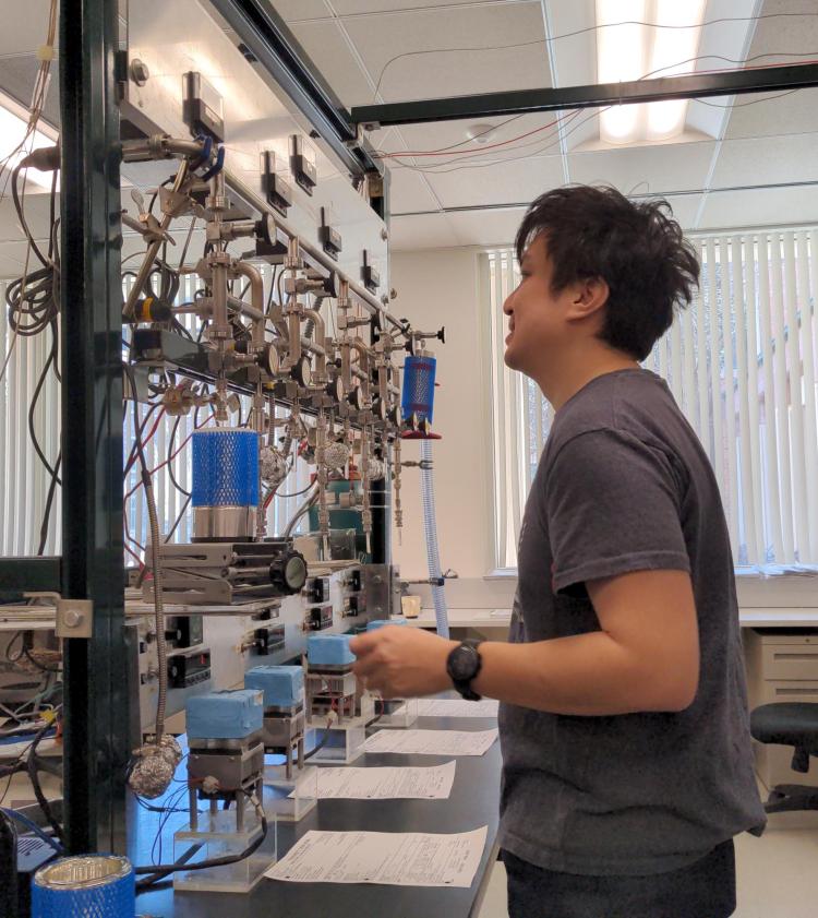 Profile view of Michael Dyonisius facing a tall rack of equipment for preparing radiocarbon samples