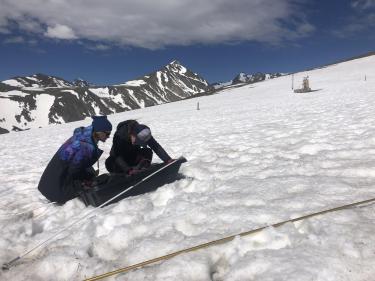 Group members Siobhan Ciafone and Nicole Scott setting up the ground penetrating radar on a snowy slope in Niwot Ridge saddle catchment, with jagged mountain peaks behind. Photo credit Kate Hale