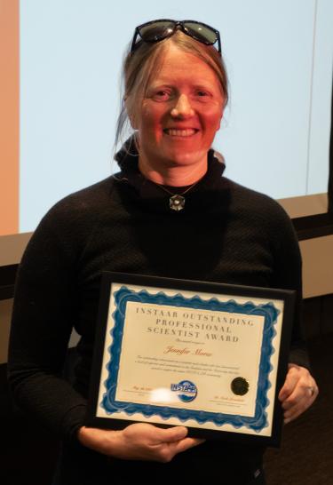 A female scientist in a black outdoor layer poses with a plaque