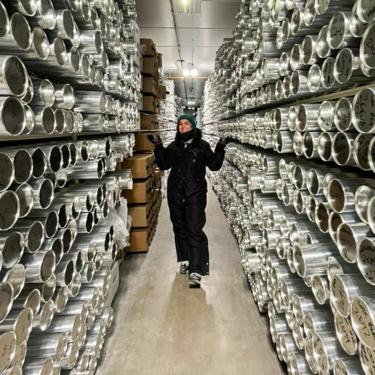 A woman in winter clothing poses in the aisle between racks of metal tubes