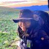 Airy Peralta - wearing a floppy hat, puffy jacket, and backpack - stands on alpine tundra