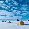 Yellow tents recede into the distance on a vast expanse of flat ice beneath a blue sky and fluffy clouds