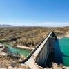A sun-baked dam holds back aquamarine water amidst a scrubby desert landscape