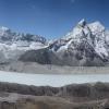A pale blue alpine lake lies among rocky slopes beneath snow-capped peaks