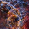 Wispy vaporous orange, blue and red clouds swirl among luminous stars against a black background