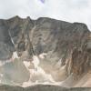 A panorama of a rocky high-altitude ridgeline studded with cliffs, snow and vegetation