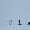 A researcher walks between a snow machine and a meteorological station amidst white out snowy conditions
