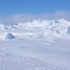 A vast expanse of snow-covered sea ice against low fluffy clouds with blue sky above