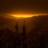 City lights are seen in the distance from the vantage point of a snowy mountainside at night.