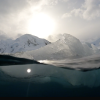 Ice floats at the surface of a cold ocean. The camera is half-submerged, showing both above and under water.