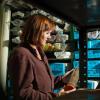 Roth looks down at a lake core, sheathed in a plastic case, that she is holding. Behind her, more cores are stacked on metal shelves.
