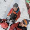 Overhead view of three smiling Antarctic researchers wearing red coats, hats, and sunglasses. Michael Dyonisius grips a powered ice auger with two hands. Right next to him are Sarah Shackleton and Bernhard Bereiter. Photo taken in austral summer of 2015-2016. Photo overlain with text saying: Meet Michael Dyonisius, INSTAAR postdoc and expert in greenhouse gases, radiocarbon, and ice cores.