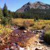 Two mountain streams come together, one with rusty red acid rock drainage