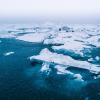 Fresh white snow falls on glacier ice floating in dark blue water