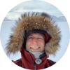 Jonathan Raberg, with a fur-lined hood, stands on a snowy arctic landscape