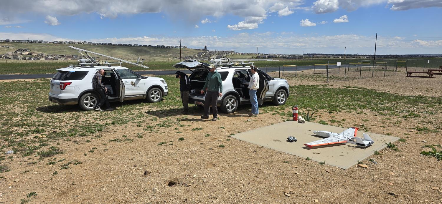 IRISS crew in front of two tracker vehicles prepare to fly the RAAVEN sUAS, lying on the ground to the right