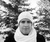 Fatemah in a hat and scarf with snow-covered pine trees in the background